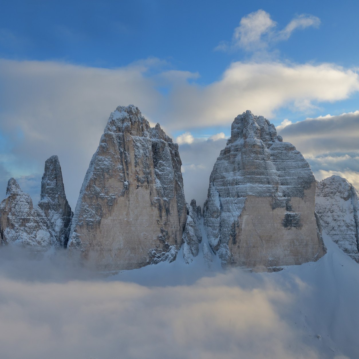 De tre tindene Tre Cime di Lavaredo med nysnø, som stiger opp av et hav av skyer