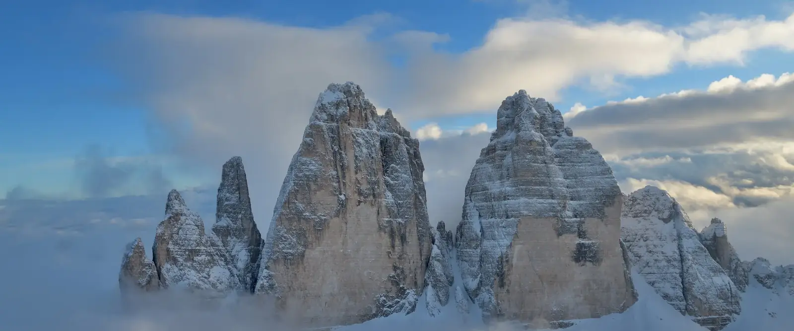 De tre tindene Tre Cime di Lavaredo med nysnø, som stiger opp av et hav av skyer